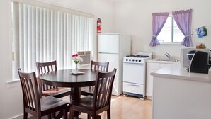A compact kitchen with a stove, sink, and refrigerator. There is a dining table with chairs and a vase with flowers. - Somass Motel (Port Alberni)