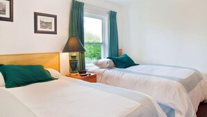 A hotel room with two beds, a nightstand with a lamp, and a window with curtains. - Somass Motel (Port Alberni)