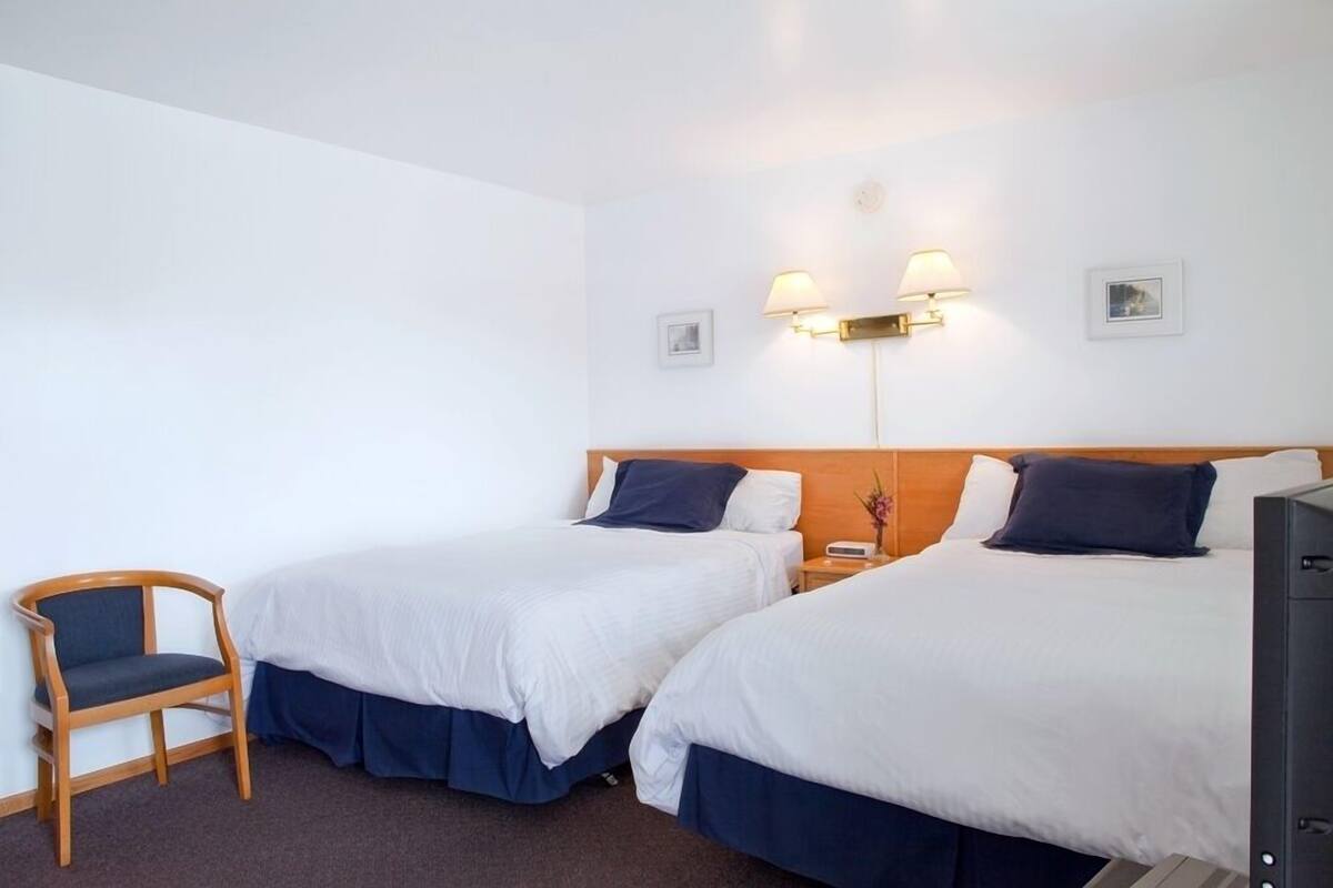 A hotel room with two single beds, a wooden chair, a desk, and two wall-mounted lamps.