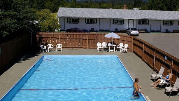 A rectangular pool with clear blue water, surrounded by white lounge chairs and a wooden deck. - Somass Motel (Port Alberni)