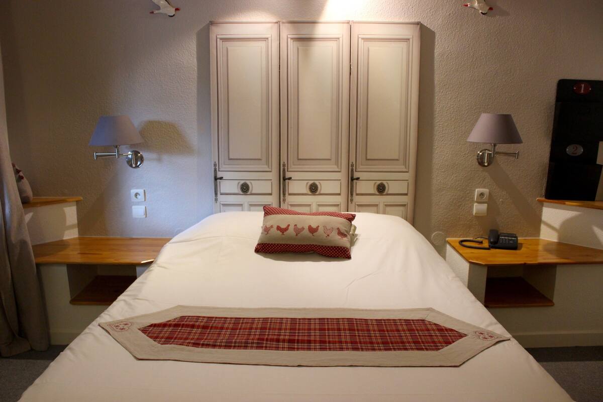 A hotel room with a bed, two bedside tables, a lamp, a telephone, and a wardrobe.