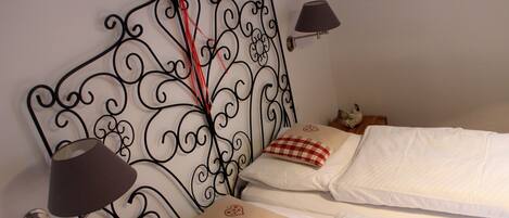 A bed with a metal headboard, white bedding, and a red and white checkered pillow.
