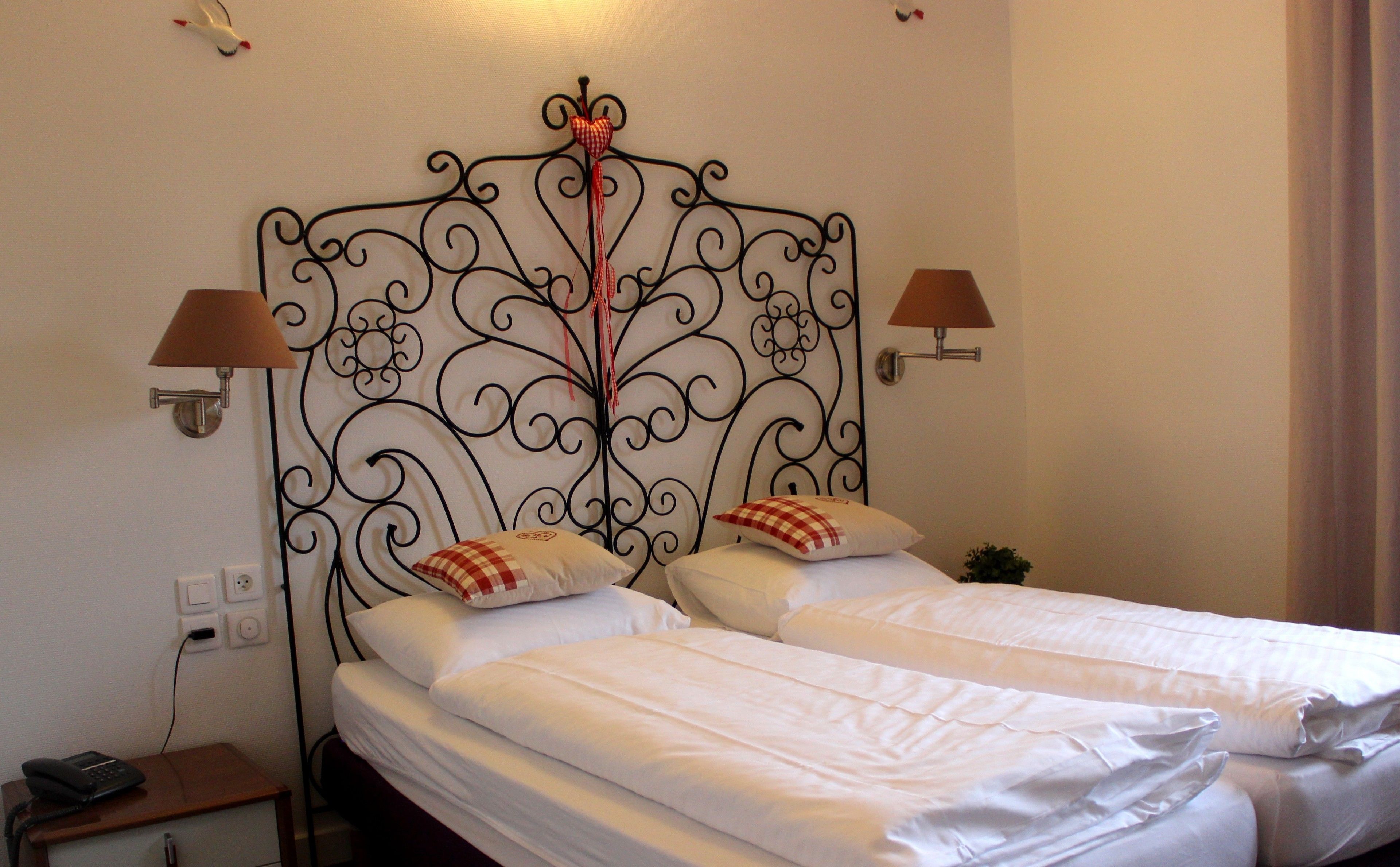 A double bed with a decorative metal headboard, two bedside lamps, and a small bedside table with a phone.