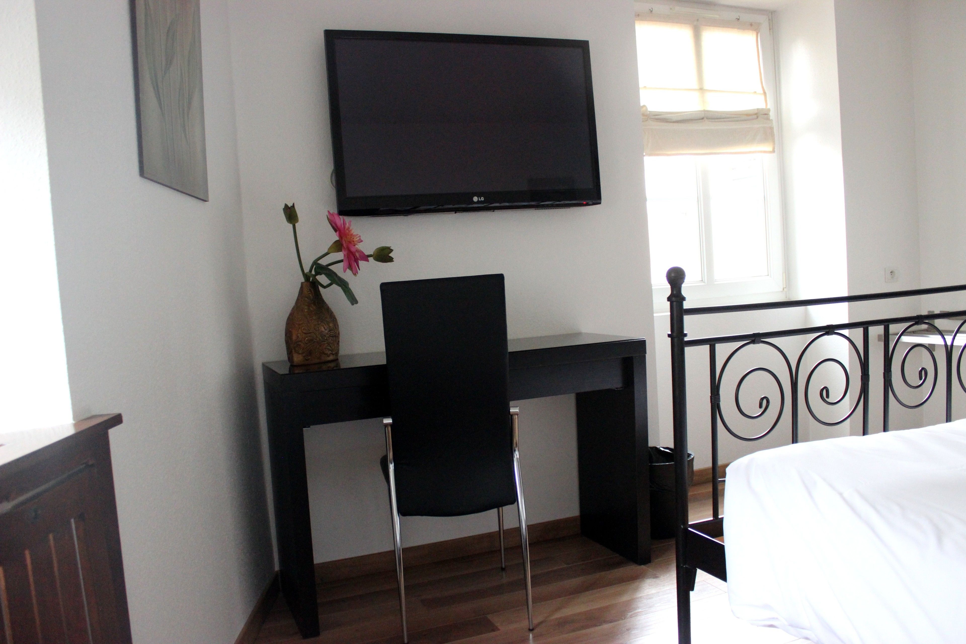 A bedroom with a bed, a desk with a chair, a television, and a window with curtains.