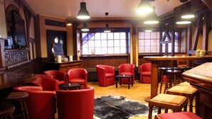 Zona de bar con asientos rojos, mesas de madera y un tapete blanco y negro en el suelo.