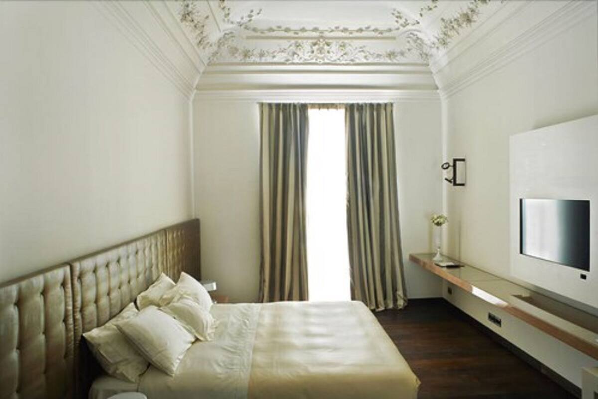 Un dormitorio con una cama grande, un televisor montado en la pared y una ventana con cortinas.