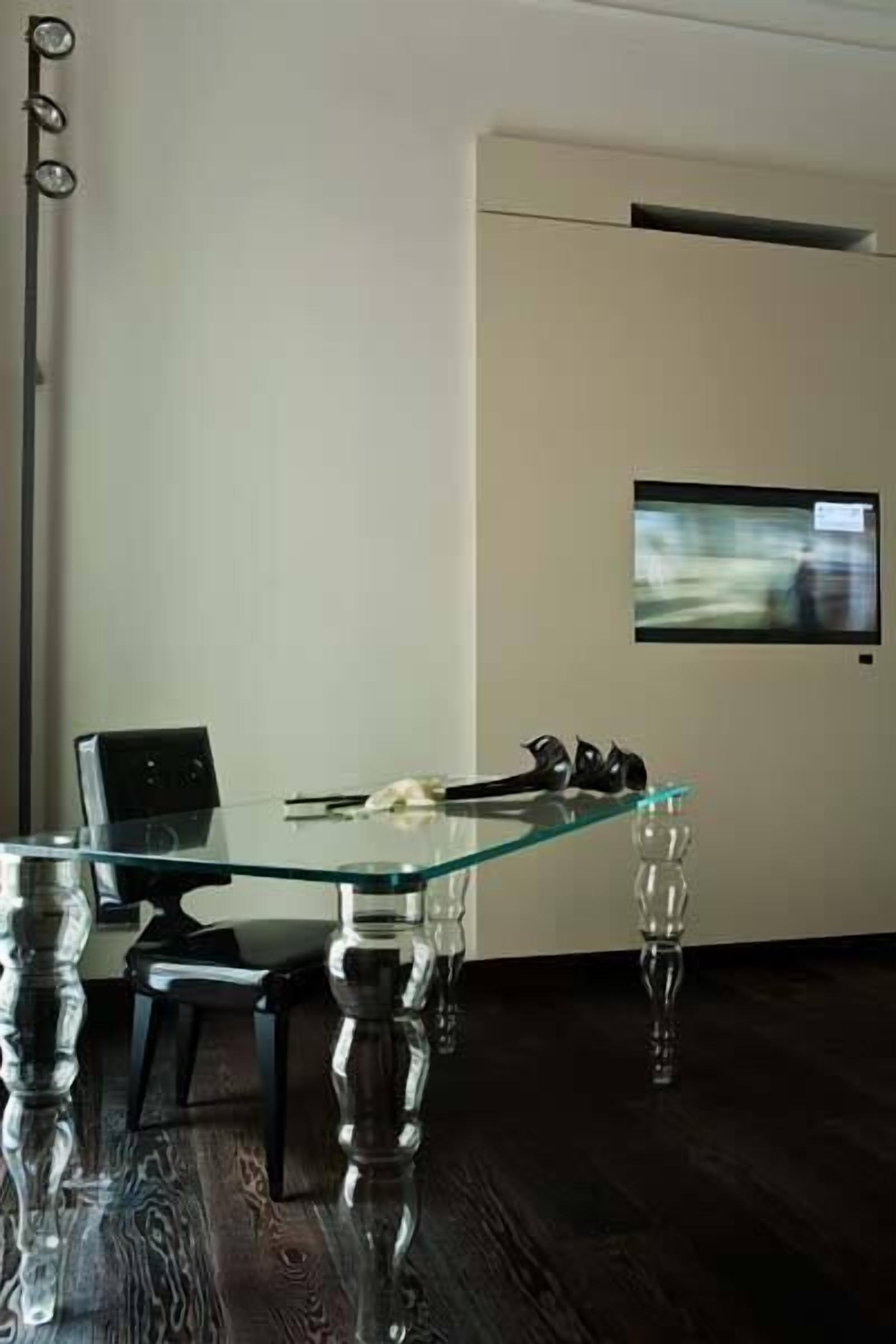 Ein moderner Konferenzraum mit Glastisch, schwarzen Stühlen, einem Laptop und einem flach an der Wand montierten Bildschirm.