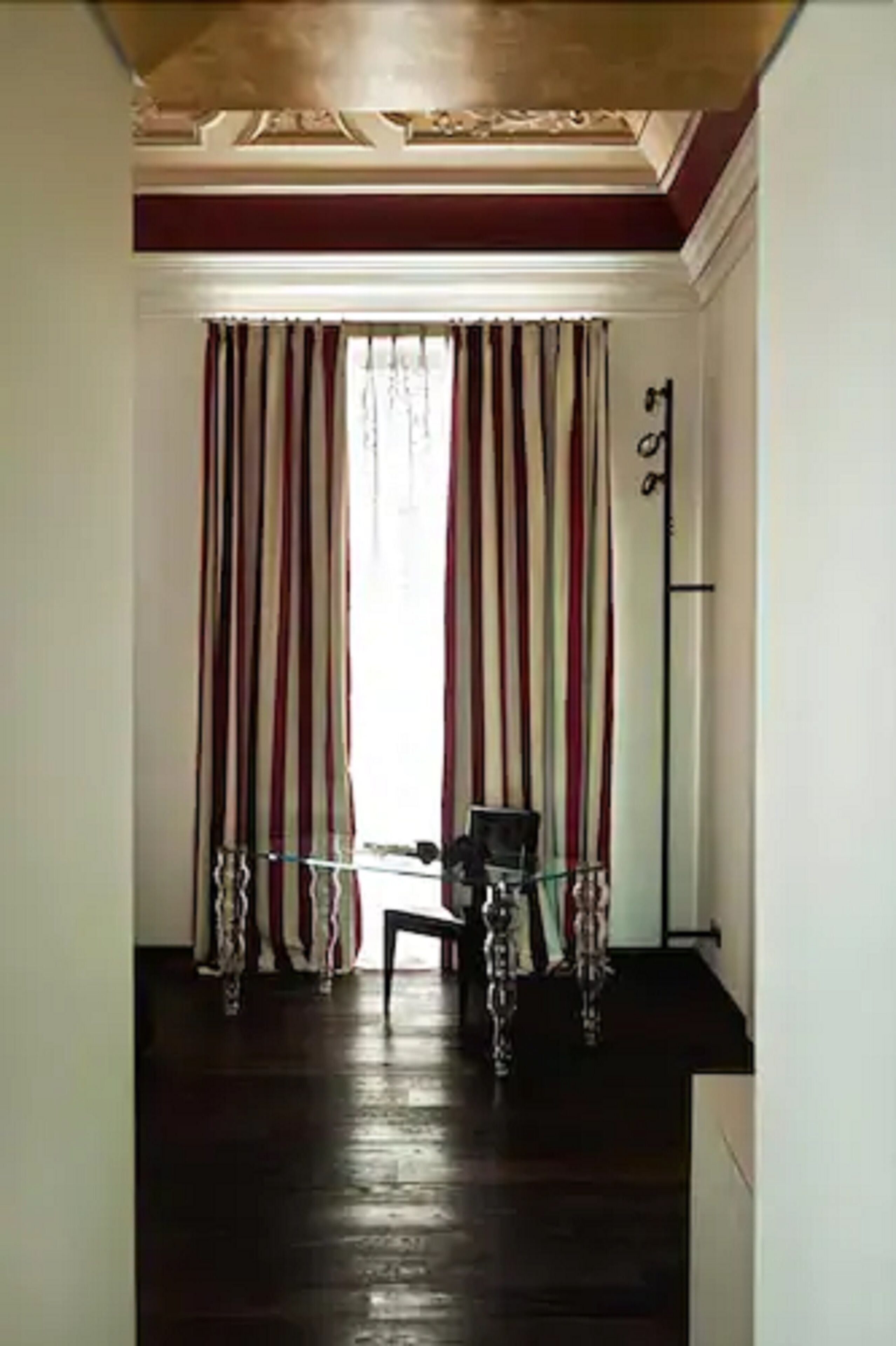 Un pasillo con piso de madera, cortinas a rayas y una pequeña mesa con una silla.