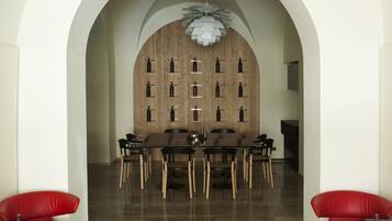 A modern dining area with a wooden wall, a chandelier, and red seating.