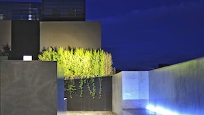 A modern outdoor area with a concrete wall, a small water feature, and a well-lit pathway. - Romano House (Catania)