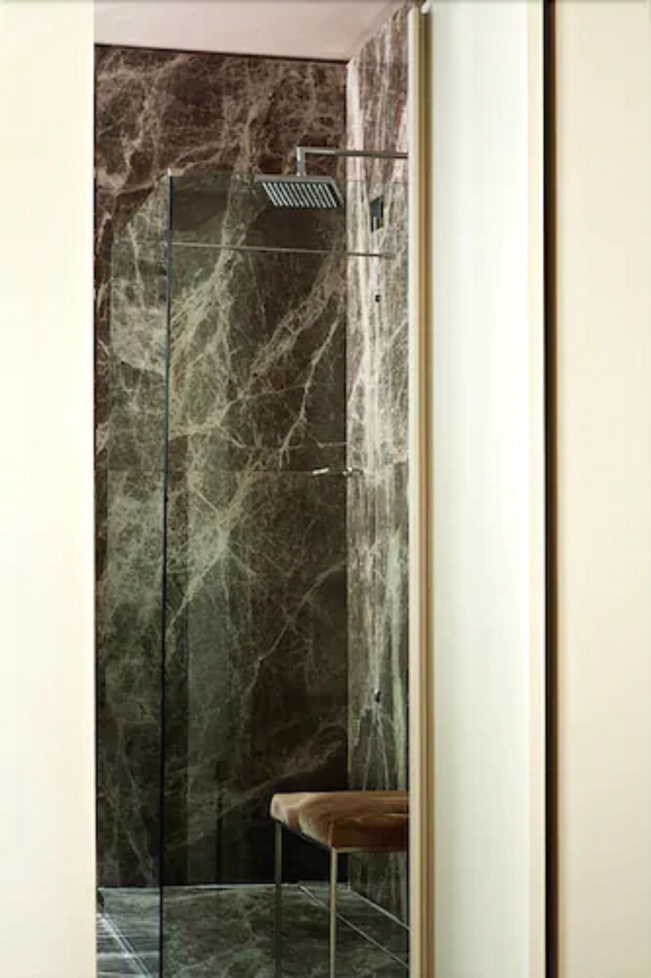 A modern bathroom with a glass-enclosed shower, marble walls, and a wooden bench.