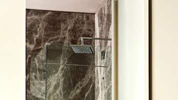 Ein modernes Badezimmer mit einer gläsernen Dusche, Marmorwänden und einer Holzbank.