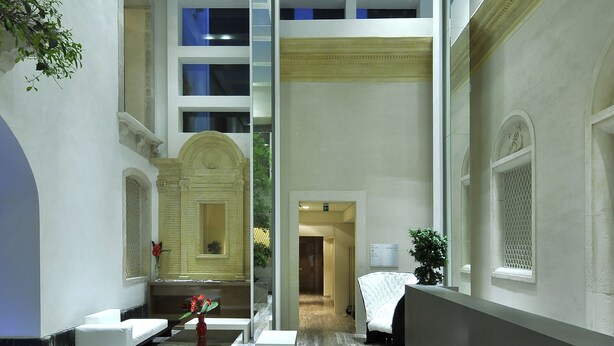 A hotel lobby with a modern design, featuring a marble floor, a central seating area, and a decorative archway. - Romano House (Catania)