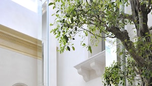 A modern interior with a white chair, a glass table, and a tree. - Romano House (Catania)