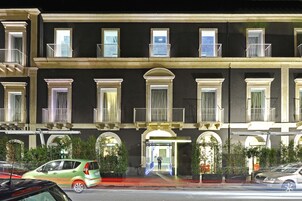 Un edificio a più piani con facciata scura, numerosi balconi e un ingresso ben illuminato.