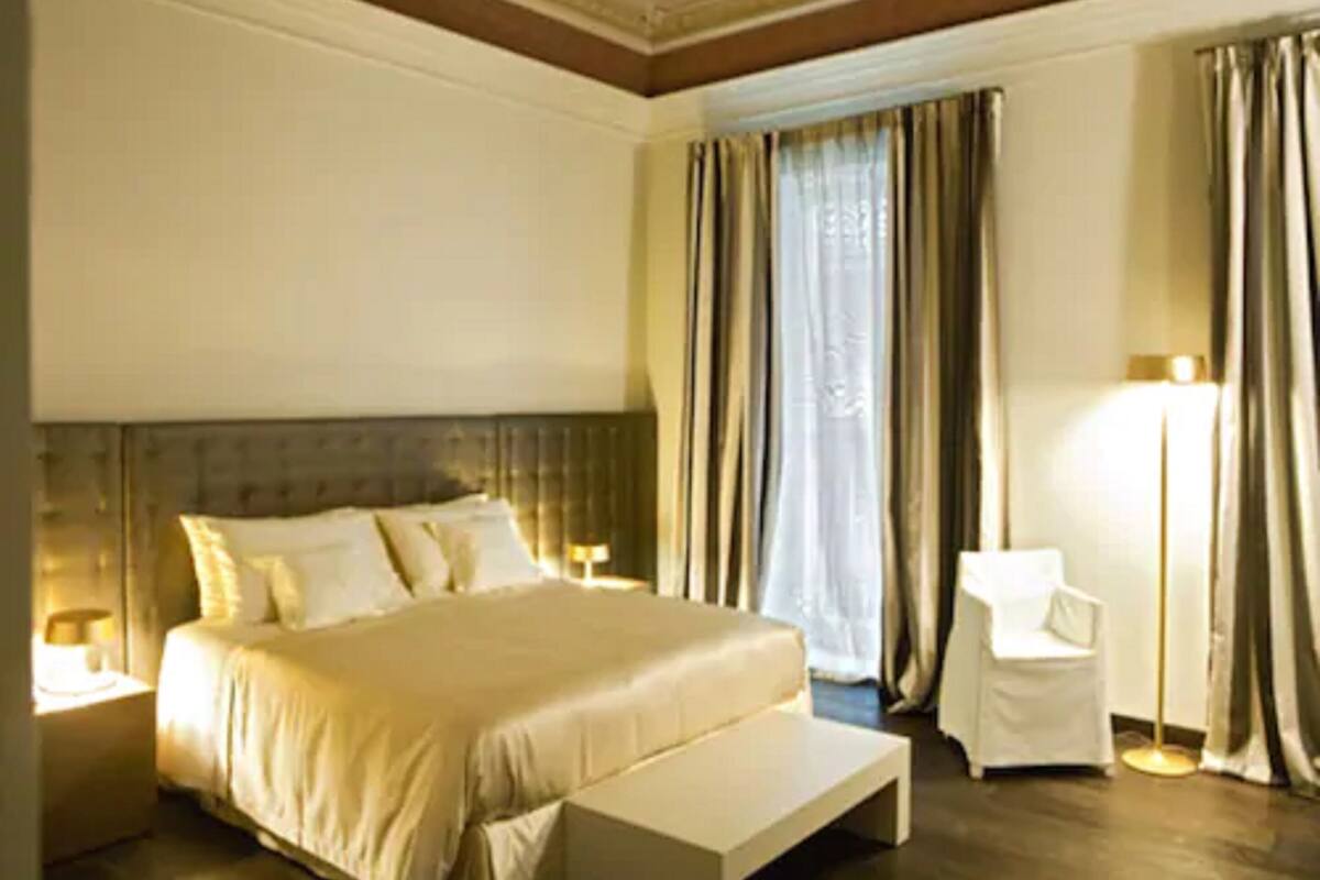 Una habitación de hotel con una cama grande, una mesita de noche, una silla y una lámpara de pie.