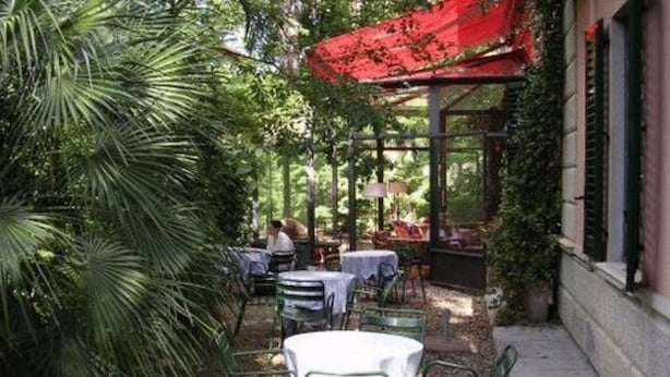 An outdoor patio with tables and chairs, surrounded by greenery and a red awning. - Classic Hotel (Florence)