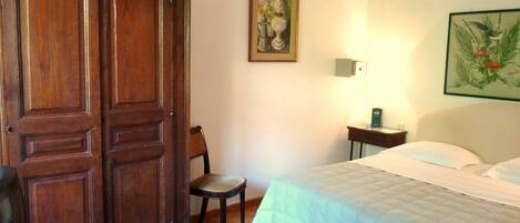 A bedroom with a bed, a wooden wardrobe, a chair, a nightstand, and a wall-mounted lamp.