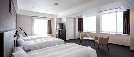 A hotel room with two beds, a desk, a chair, a television, and large windows.