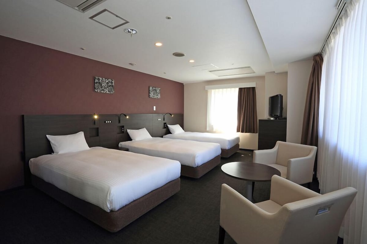 A hotel room with three beds, a TV, a desk, and a chair.
