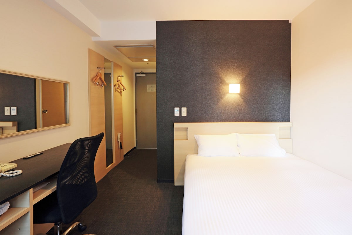 A hotel room with a bed, a desk, a chair, and a mirror.