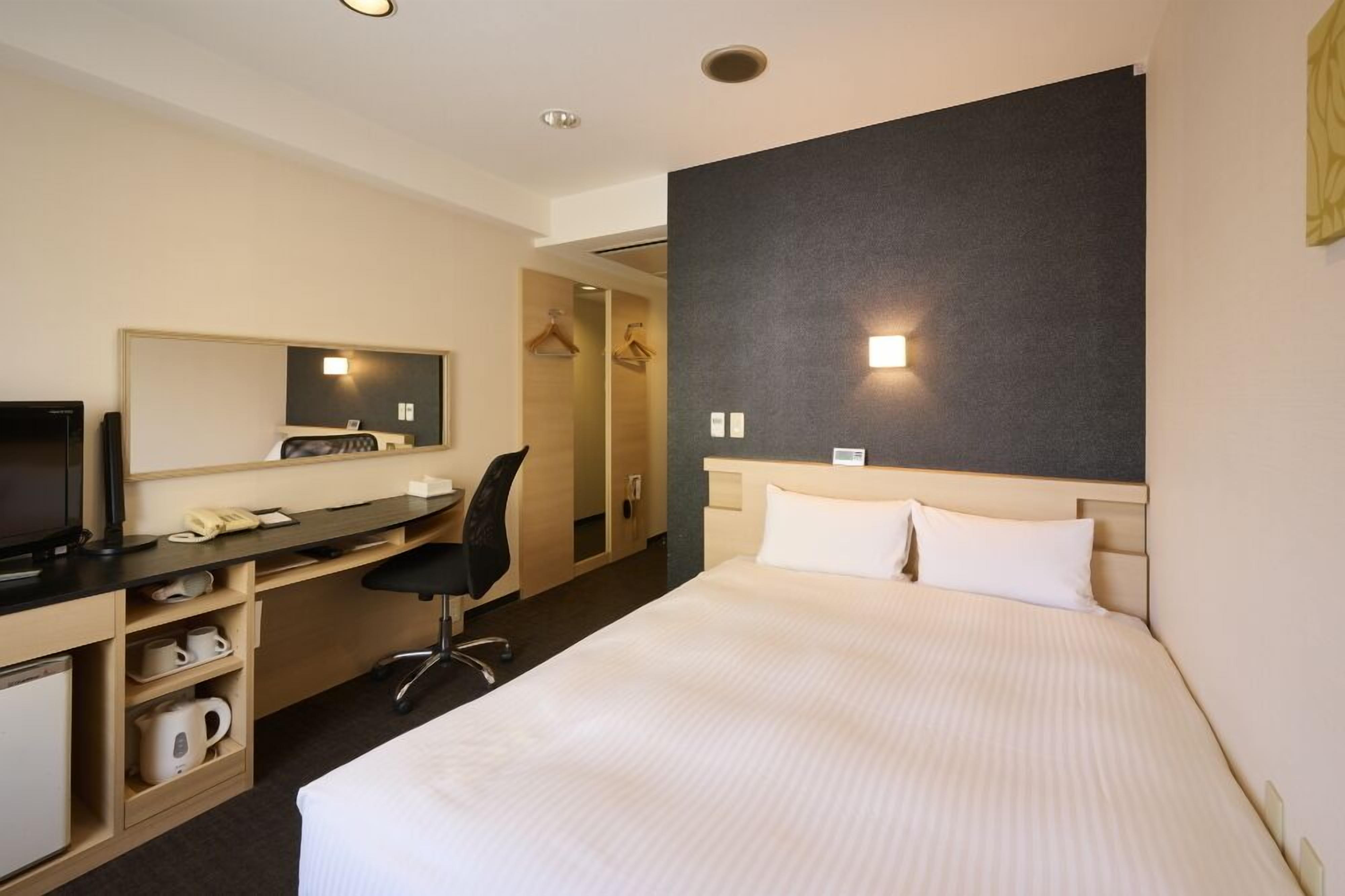 Una habitación de hotel con cama, escritorio con computadora, silla, televisor y armario.