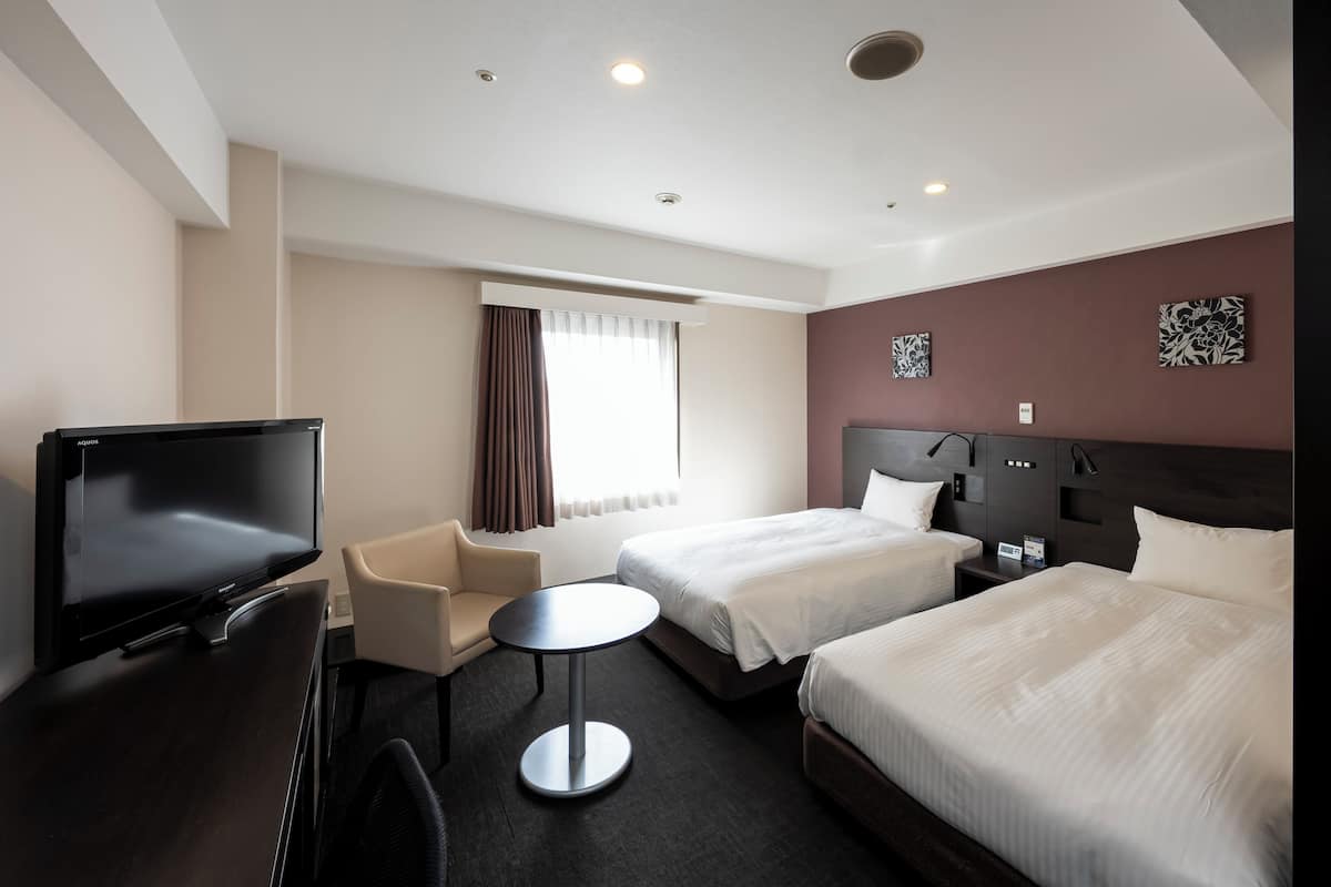 A hotel room with two beds, a TV, a desk, and a chair.