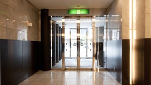 A modern lobby with a glass entrance, a green exit sign, and a tiled floor.