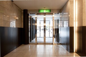 Um hall moderno com entrada de vidro, uma placa de saída verde e piso ladrilhado.