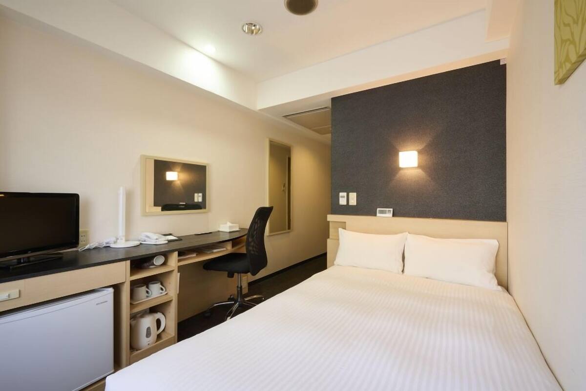 A hotel room with a bed, desk, chair, and a television.