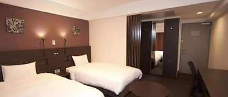A hotel room with two beds, a small round table, and a chair. There is a door leading to another room.