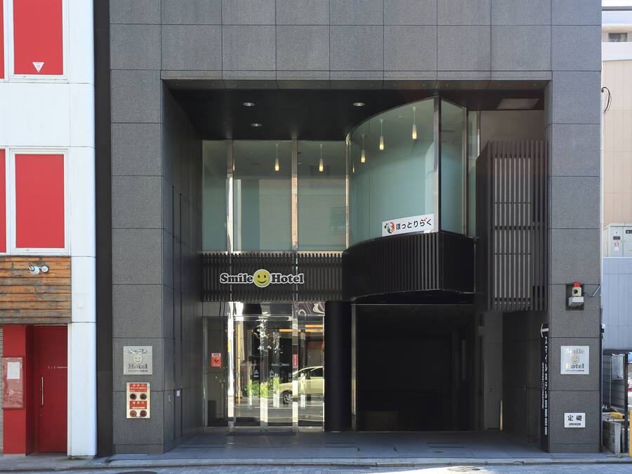 Entrada de hotel com design moderno, portas de vidro e uma placa indicando ser o Smile Hotel.