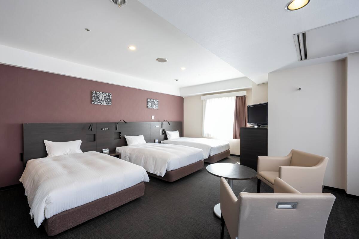 A hotel room with three beds, a TV, a desk, and a chair.