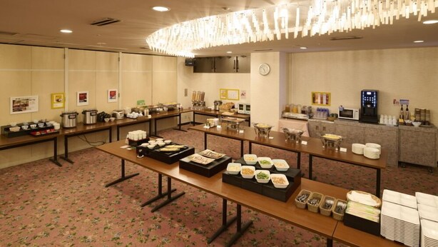 Un salón de conferencias con mesas largas dispuestas para un bufé, equipado con varias estaciones de comida y un reloj en la pared.