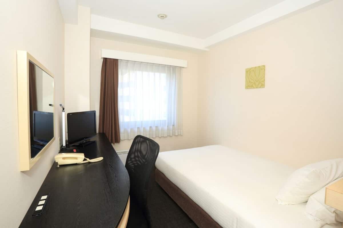 Une chambre d’hôtel comprenant un lit, un bureau avec un téléphone, une chaise, un téléviseur et une fenêtre avec des rideaux.
