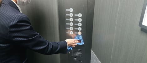 Una persona limpiando el panel de control de un ascensor con un paño azul.