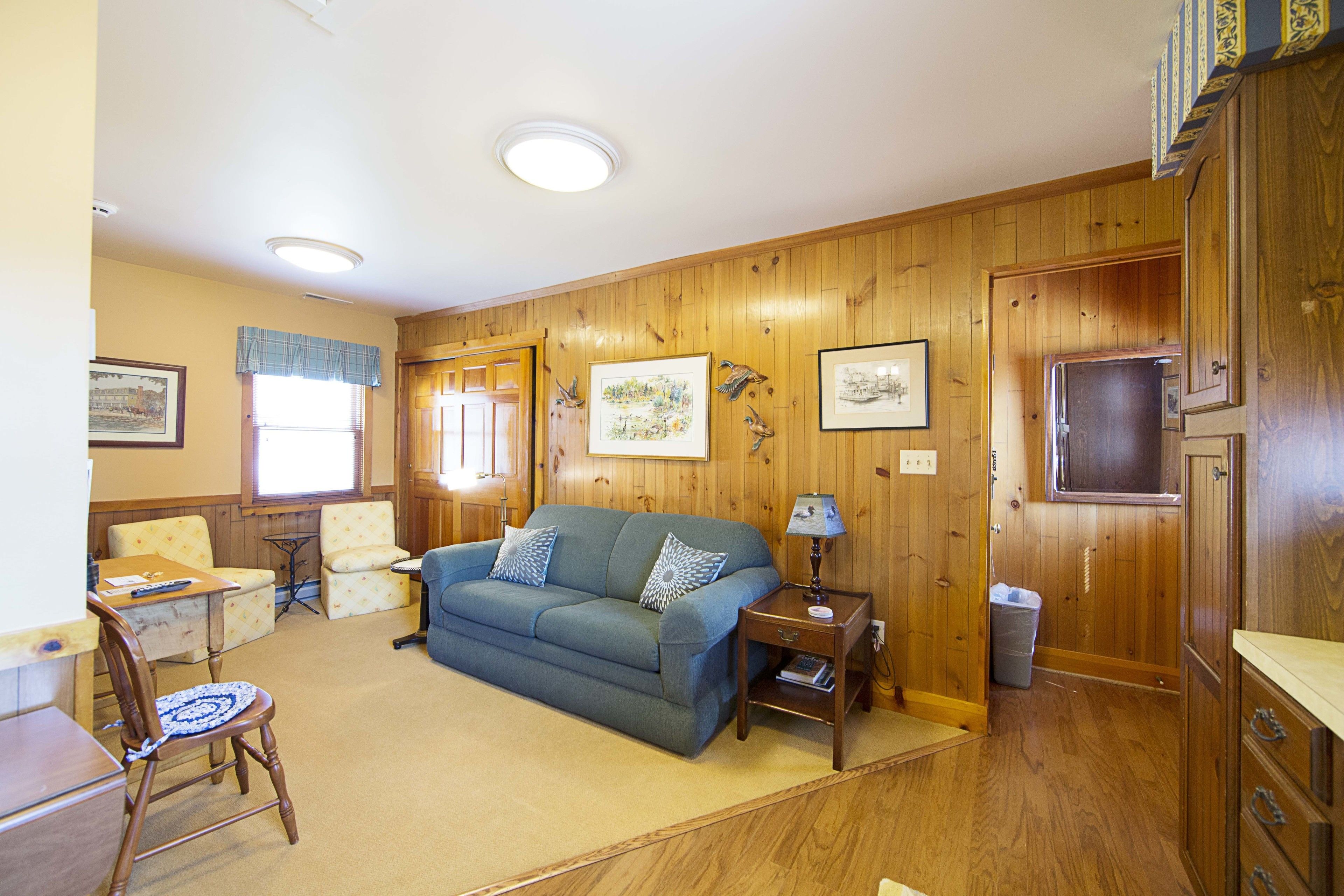 A cozy living room with a blue sofa, wooden walls, and a small table with a lamp.