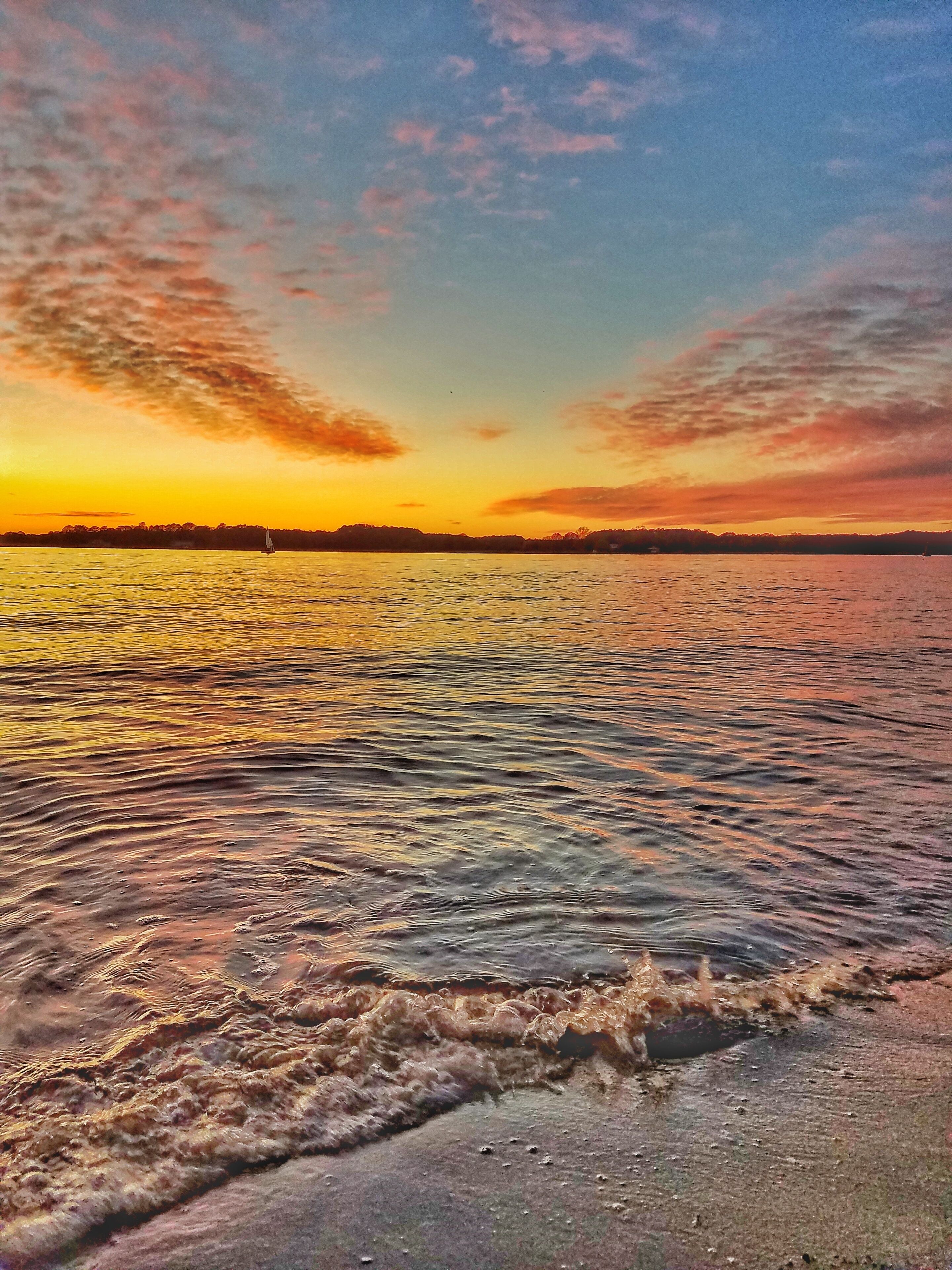 Un atardecer sobre un cuerpo de agua tranquilo, con la silueta de un velero a lo lejos.