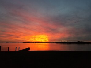A sunset over a calm body of water with a silhouette of a boat and a fence in the foreground. - Sandaway Suites & Beach (Oxford)