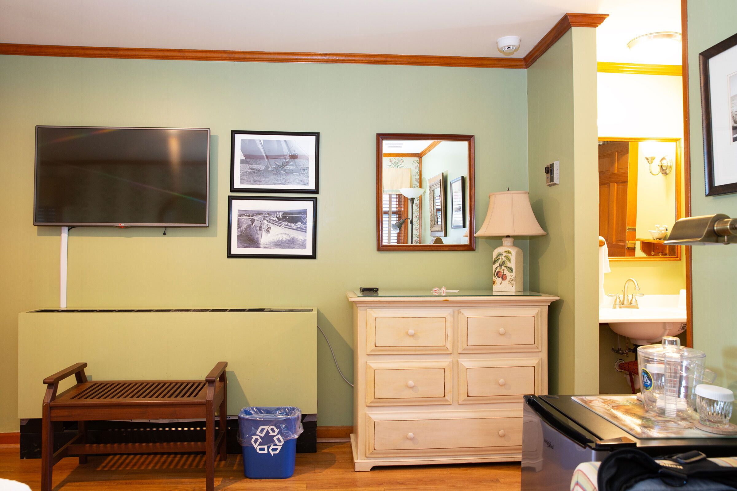 Une pièce avec un banc en bois, une commode, un téléviseur et des tableaux encadrés accrochés au mur.