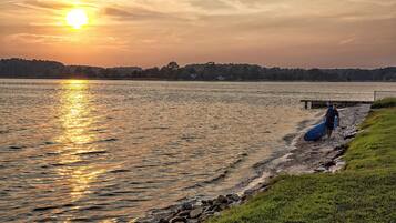 Tramonto su un lago, con una persona che trasporta un'asse da surf vicino a un pontile.