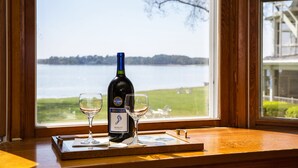 Eine Flasche Merlot und zwei Gläser auf einer Holztablett vor einem Fenster mit Blick auf einen See.