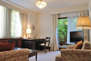 A hotel room with a desk, chair, sofa, TV, and a view of greenery outside. - Hilltop Hotel (Tokyo)