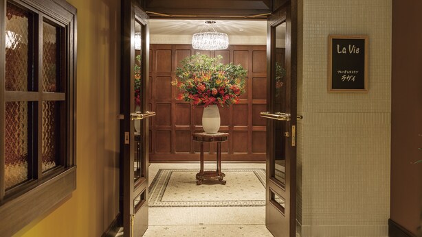 A hotel lobby with a wooden reception desk, a chandelier, and a sign that reads "La Vie." - Hilltop Hotel (Tokyo)