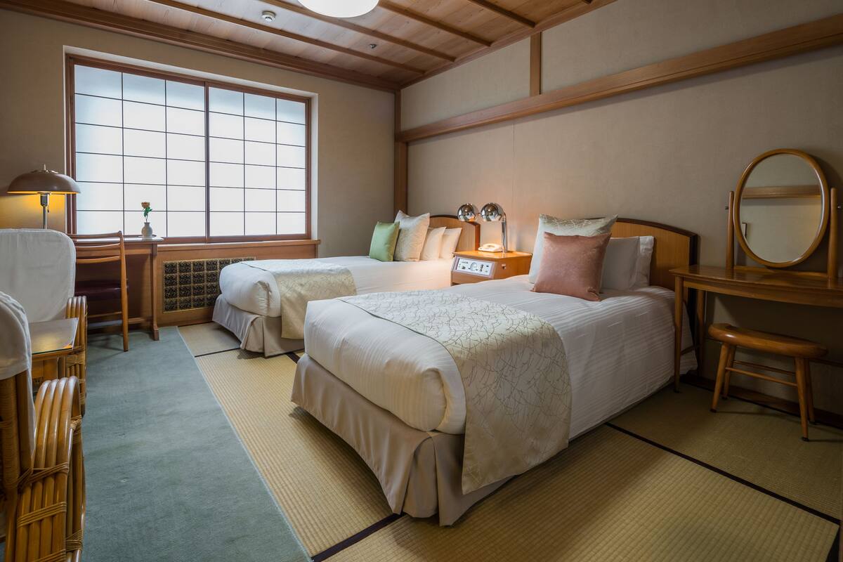 A traditional Japanese-style room with two beds, a wooden desk, a mirror, and tatami mats.