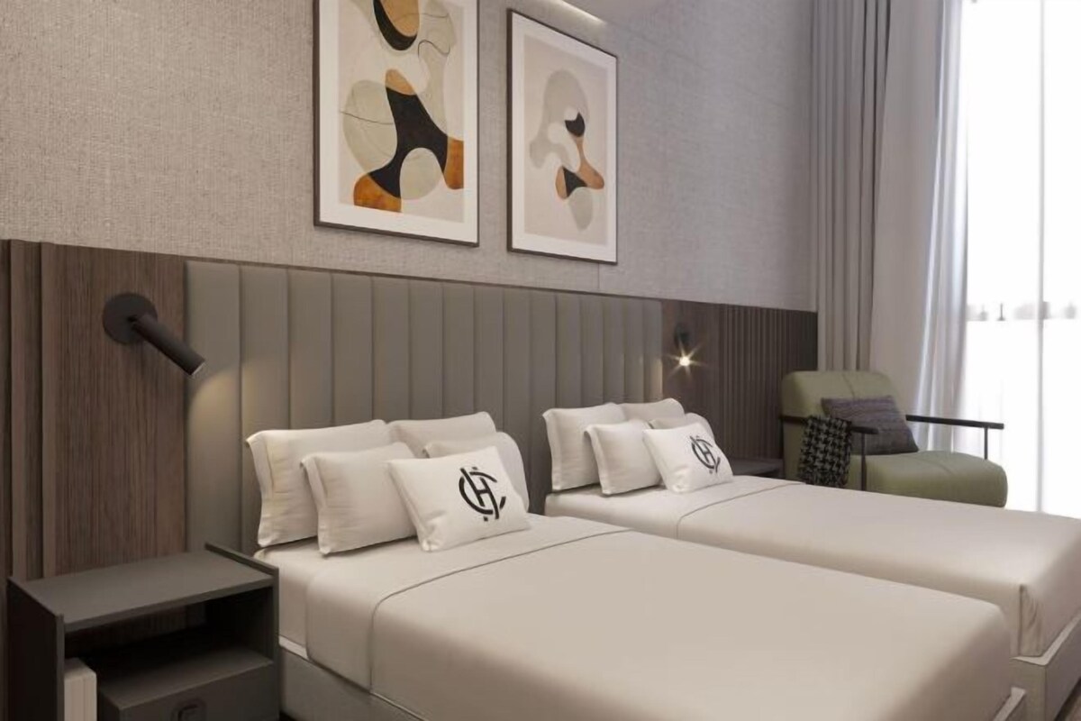 A modern hotel room with two beds, a nightstand, a chair, and abstract artwork on the wall.