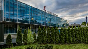 Un hôtel moderne, avec une façade en verre, un logo bien visible et un jardin bien entretenu à l’avant.