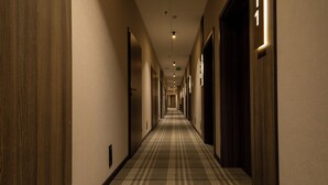 Un couloir d’hôtel avec un tapis à carreaux, des portes en bois et une rangée de luminaires le long du plafond.
