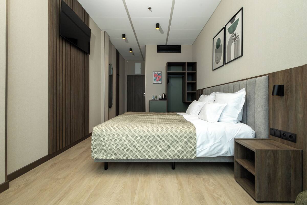Una habitación de hotel moderna con una cama grande, una mesita de noche, un armario y un espejo.