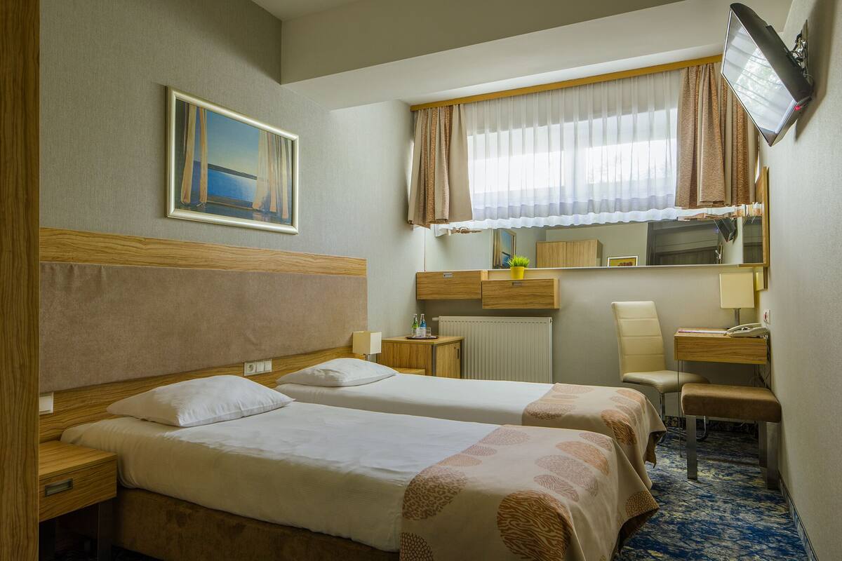 Habitación de hotel con dos camas, un escritorio, una silla, un televisor y una ventana con cortinas.
